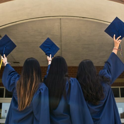 three girls in graduation gowns hold their caps in the air